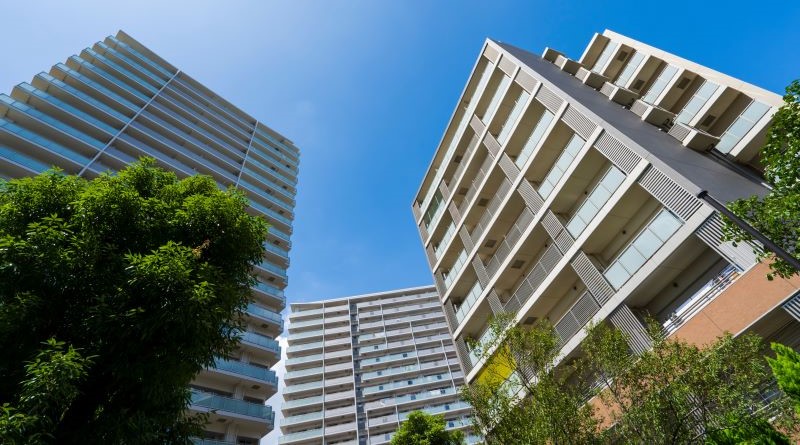 Vier Hochhäuser, die in Ballungszentren Wohnraum bieten, perspektivisch fotografiert von unten in den blauen Himmel hinein.